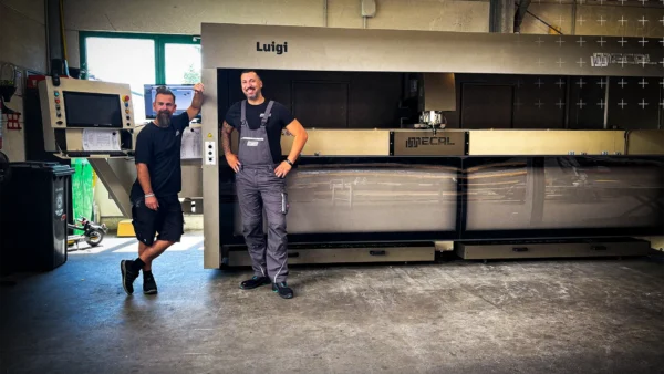 Lagerleiter Paolo Adragna und stellv. Lagerleiter Sebastian Schäfer-Stark stehen vor dem neuen CNC-Stabbearbeitungszentrum bei mejo in Düsseldorf